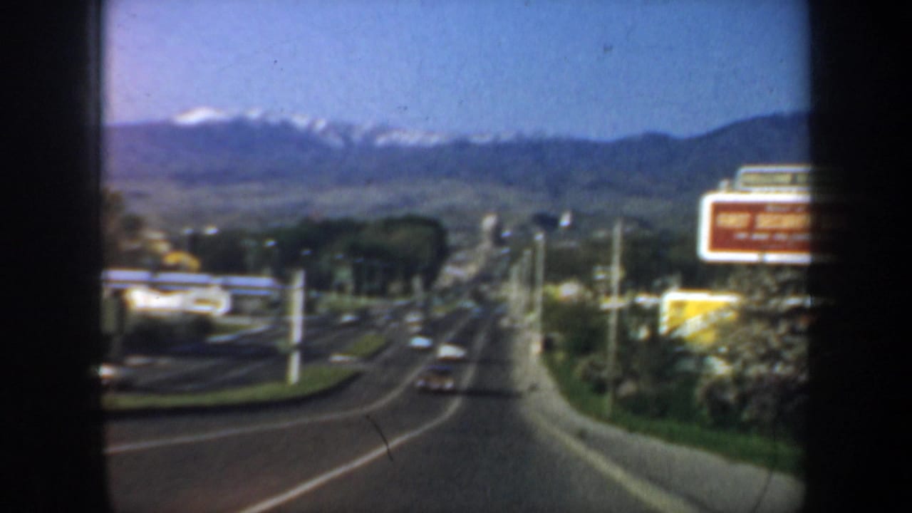 Highway descending toward hills with cars and roadside billboards.