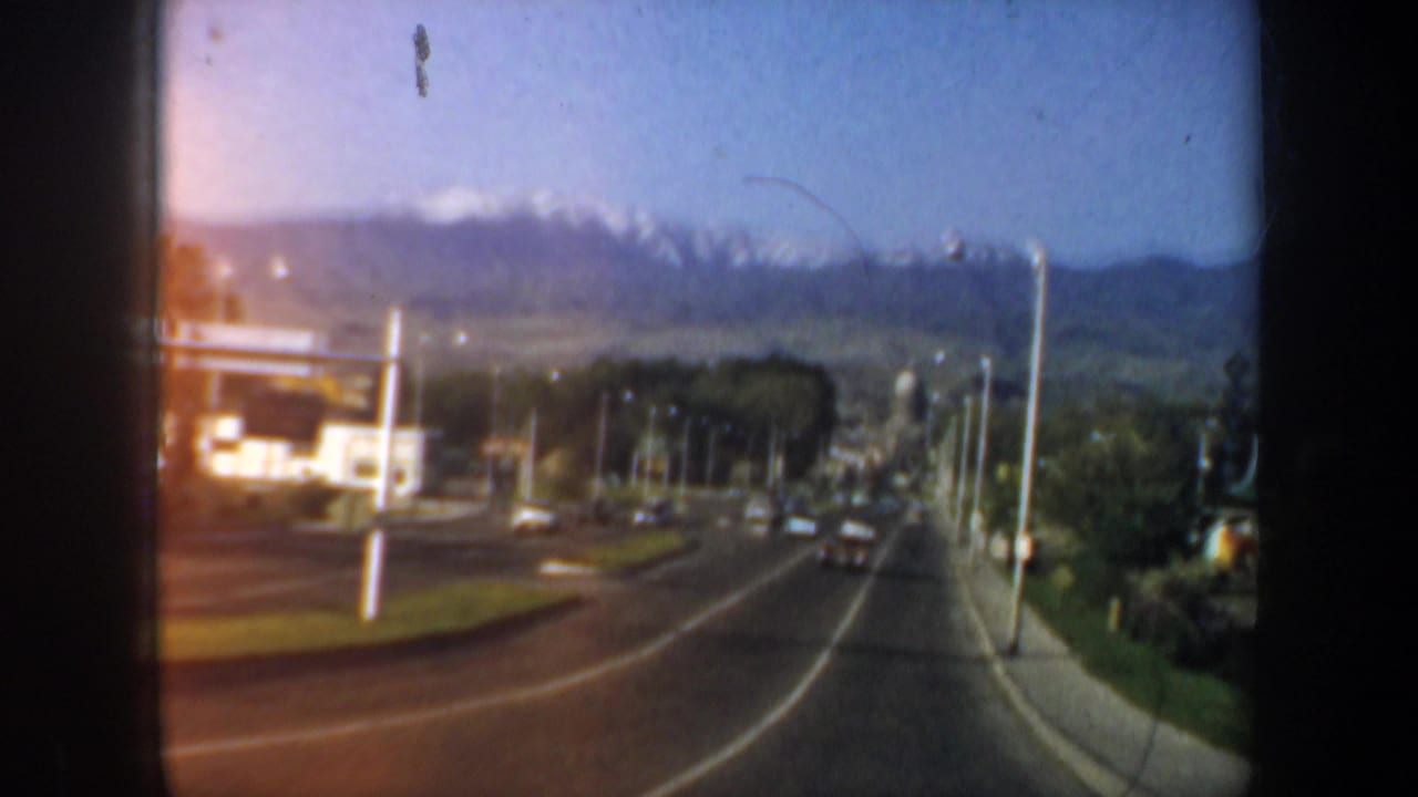 1957 Oregon home-movie view of a curving road, roadside structures, utility poles, trees, and hills in the distance.