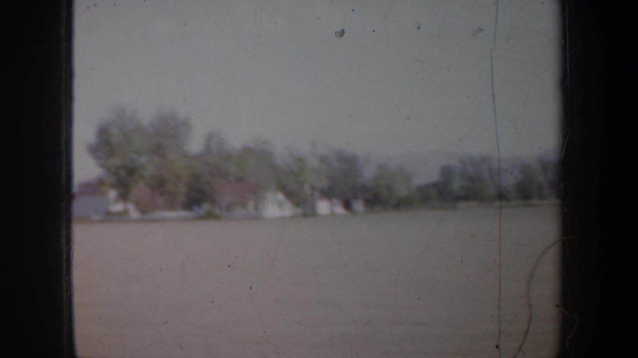Moving 8mm view near Portland in 1957, with open land in the foreground and houses partly hidden by trees.
