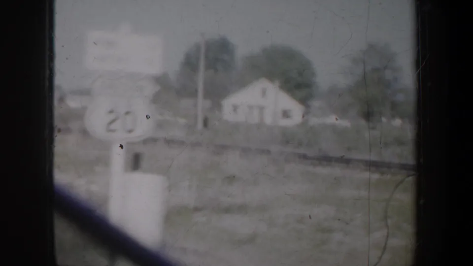 1957 Portland-area home-movie frame showing a blurred rural house, roadside marker, and dark window framing from a moving vehicle.