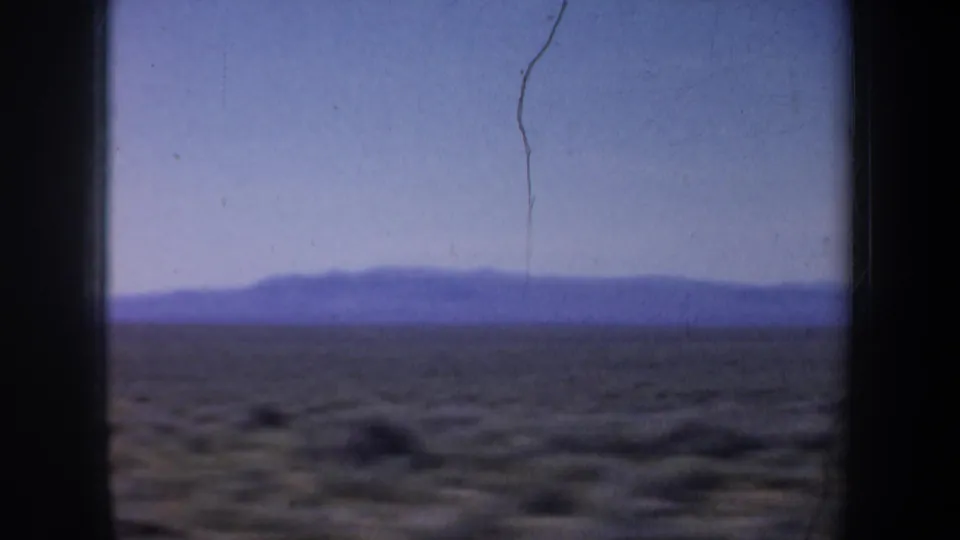 A final 1957 8mm travel frame shows dark edge framing, distant mountains, open scrub terrain, and visible film wear.