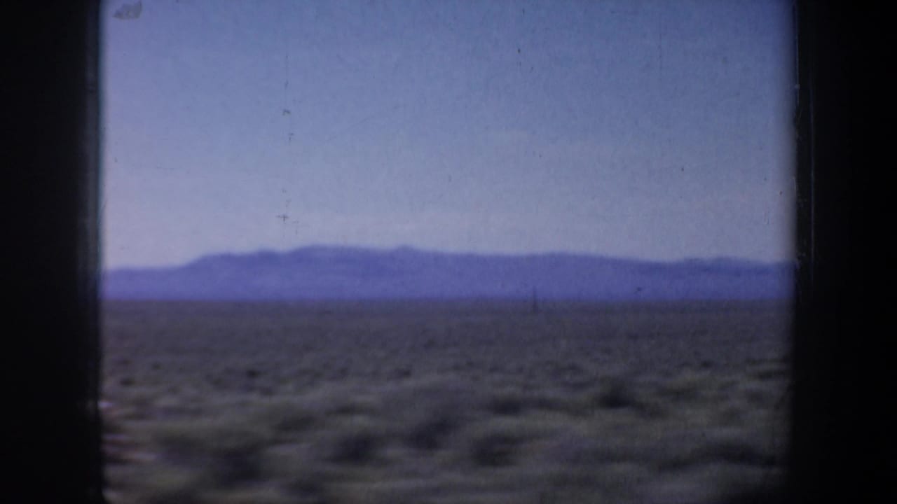 1957 8mm travel footage showing arid scrubland and low mountains framed by a dark vehicle window divider.