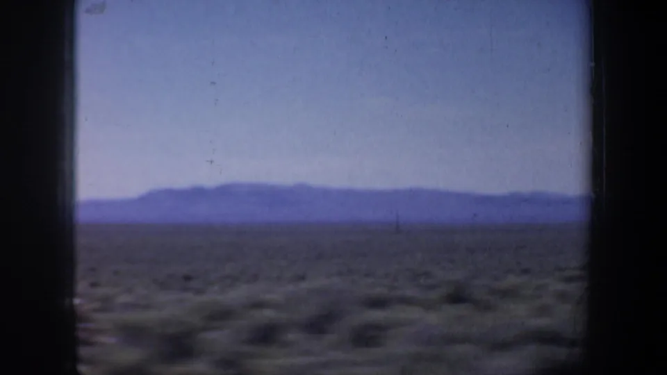 1957 8mm travel footage showing arid scrubland and low mountains framed by a dark vehicle window divider.