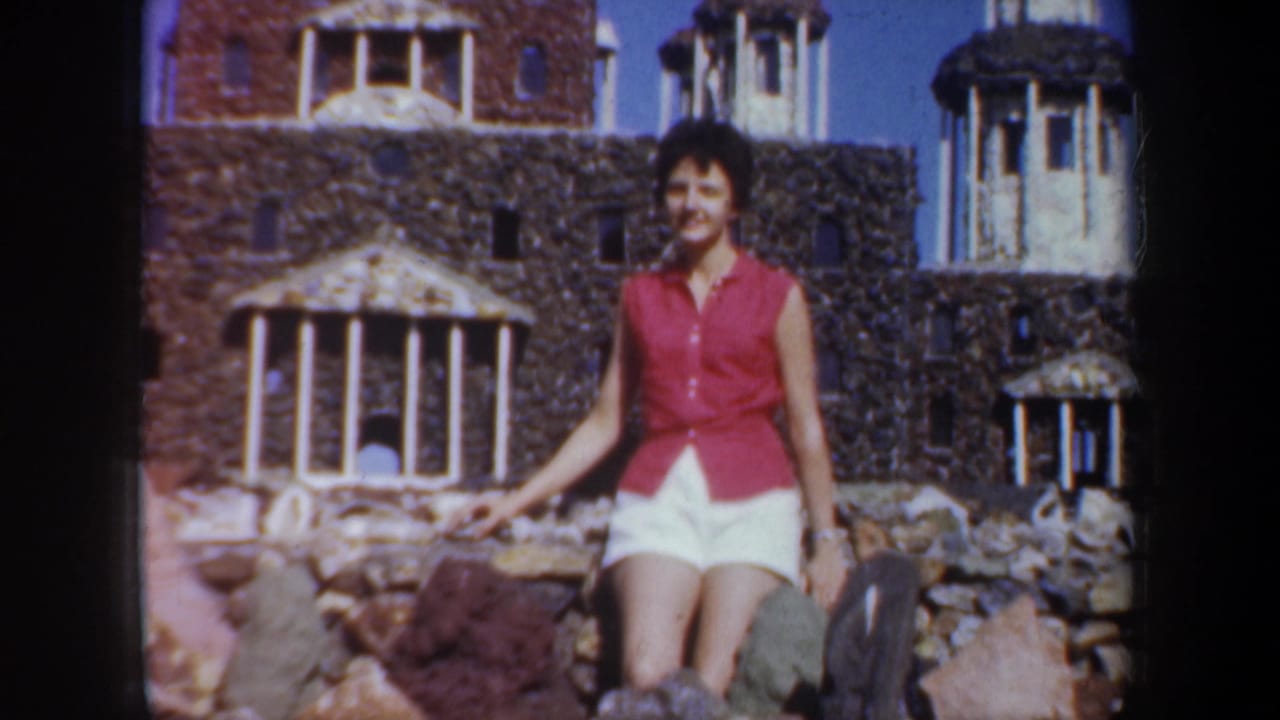 Woman in a red sleeveless top and white shorts posing among rocks before miniature buildings.