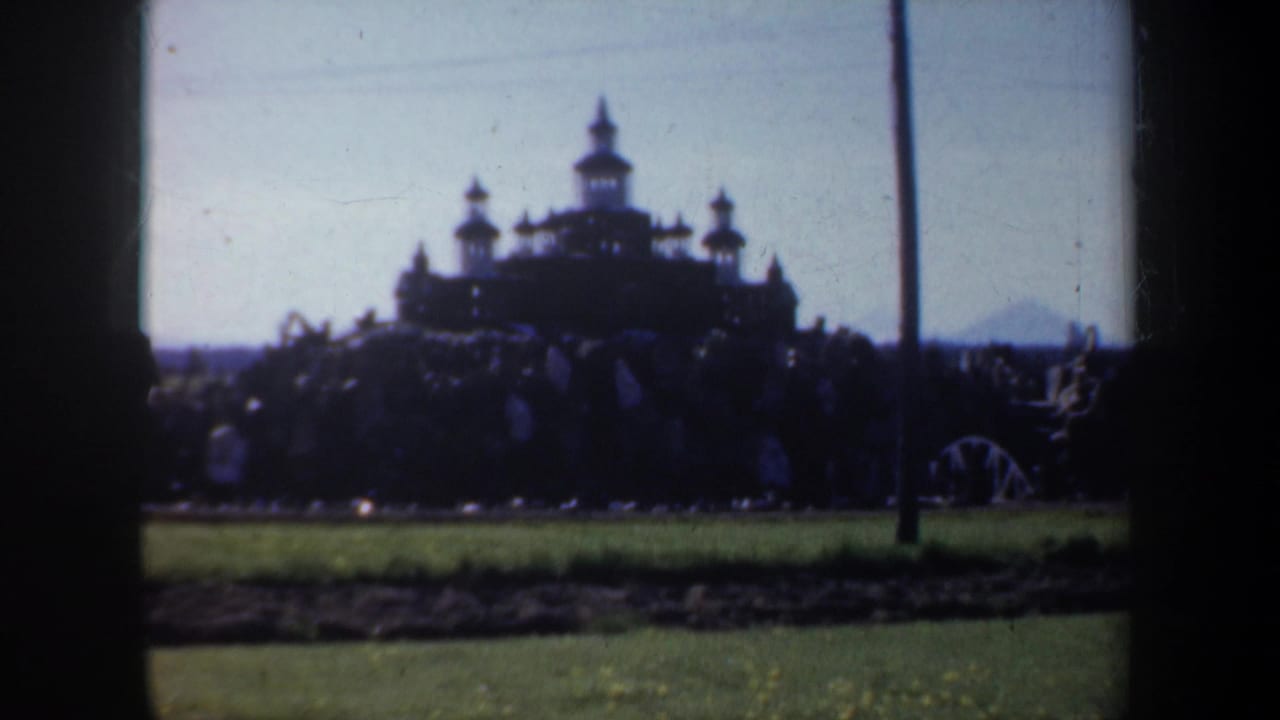 Distant dark silhouette of a turreted stone structure seen across grass.