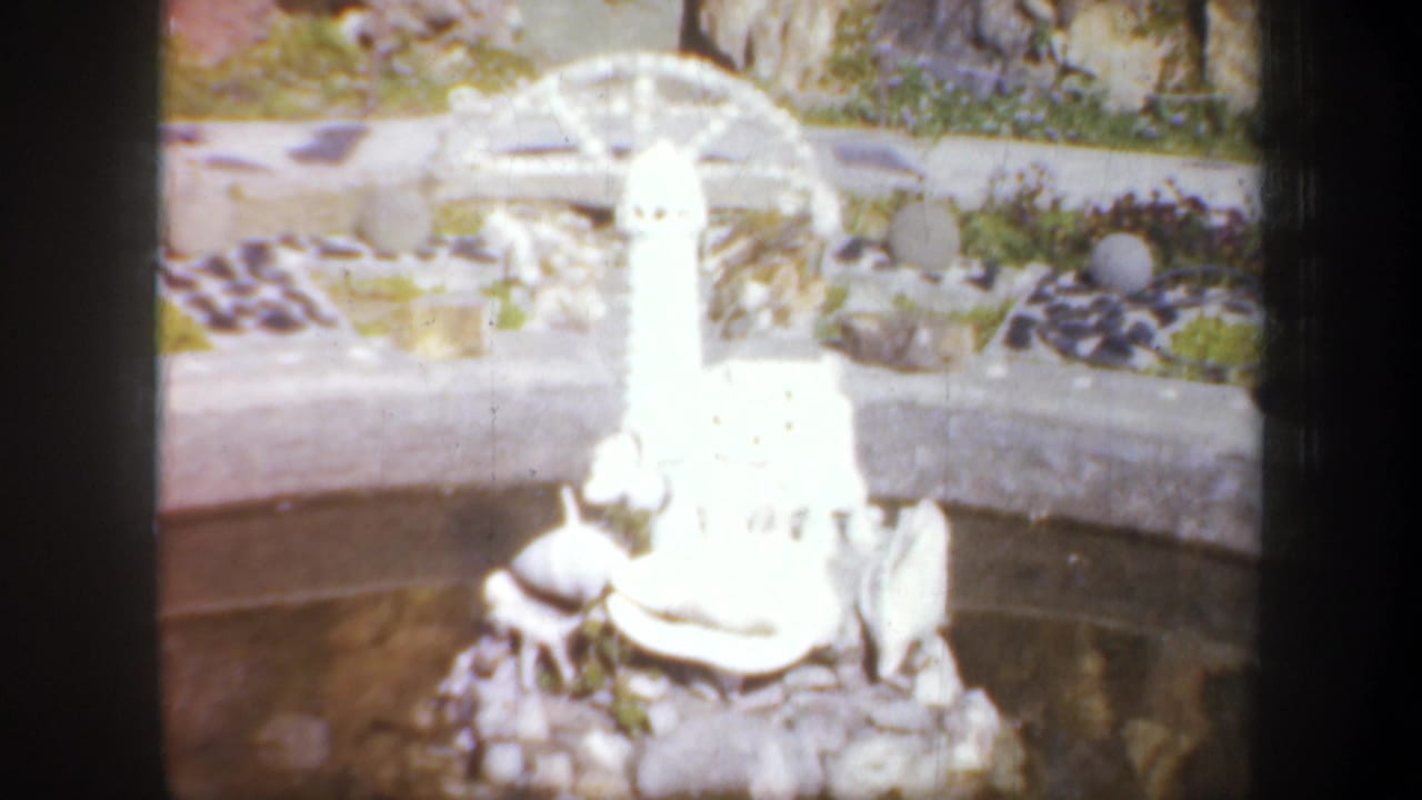 White miniature lighthouse beside a decorative pond with rocks and shells.