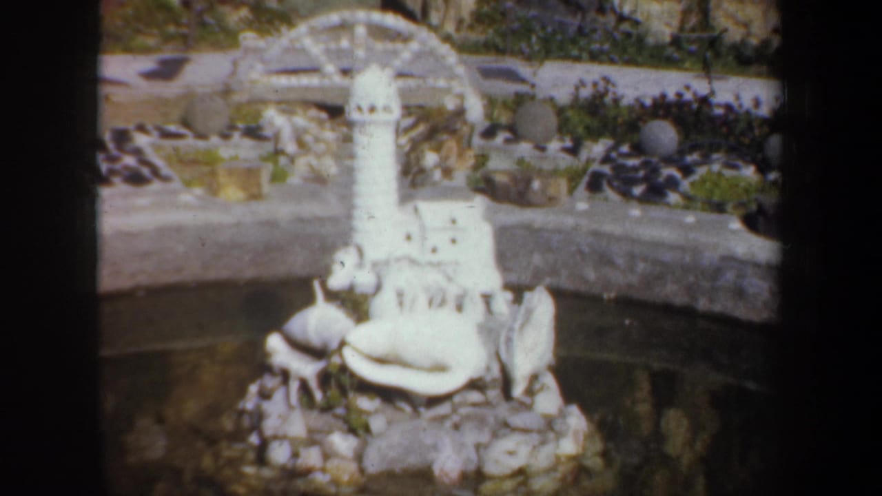 Miniature lighthouse display beside pond water and a curved stone edge.