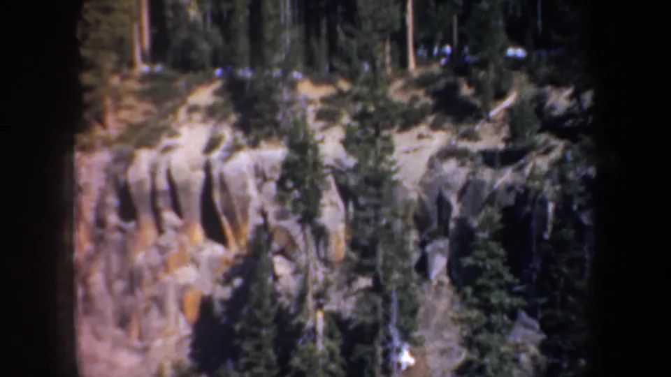 1957 Oregon 8mm frame showing a rocky canyon wall, evergreen growth, and dark projected-film edges.