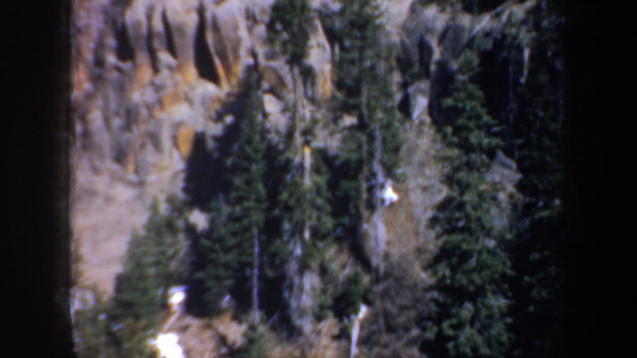 1957 8mm home-movie frame of a rocky evergreen slope near Portland, Oregon, with snow visible along the lower terrain.