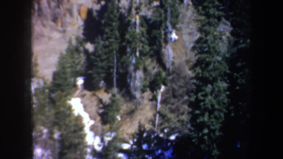 Vintage 8mm frame showing a steep forested rock face with snow streaks and dark tree cover in the supplied Portland, Oregon setting.