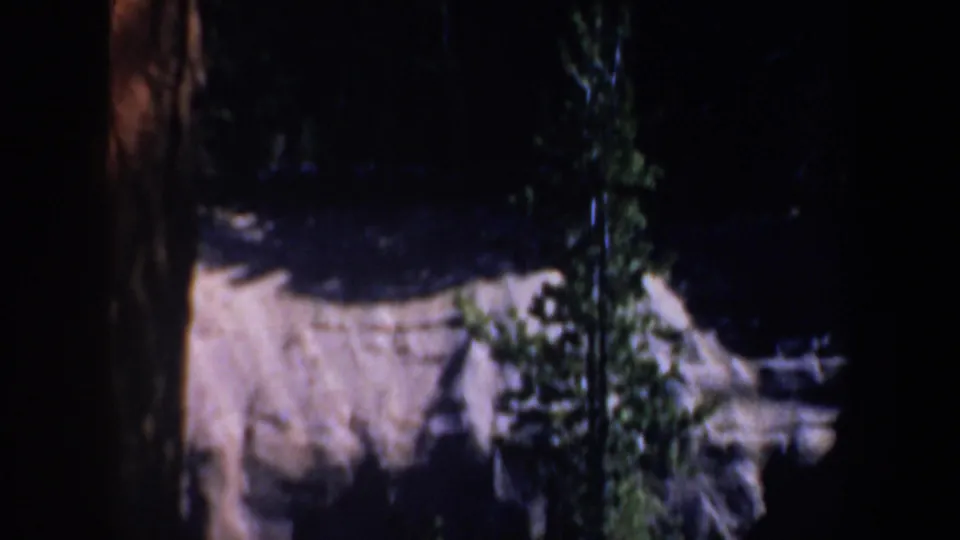 1957 Oregon mountain terrain appears through dark trees, with a pale rocky face and dense evergreen cover.
