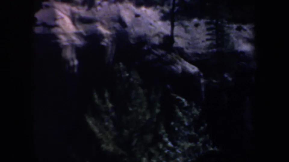 1957 Oregon 8mm frame showing dark woods, rocky or earthen ground, and a narrow bright band of snow or ice across the scene.