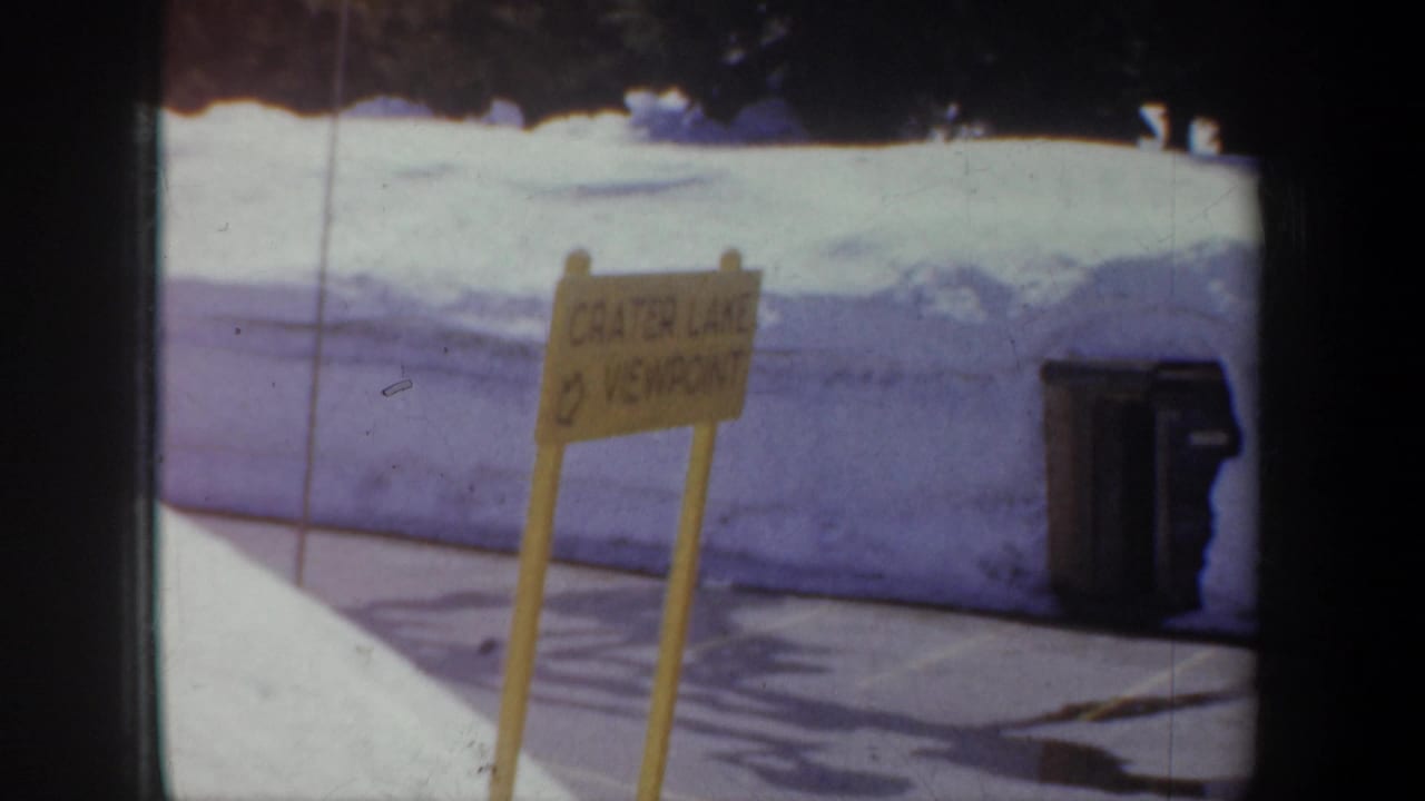 Yellow Crater Lake viewpoint sign beside snowbanks and a trash can.