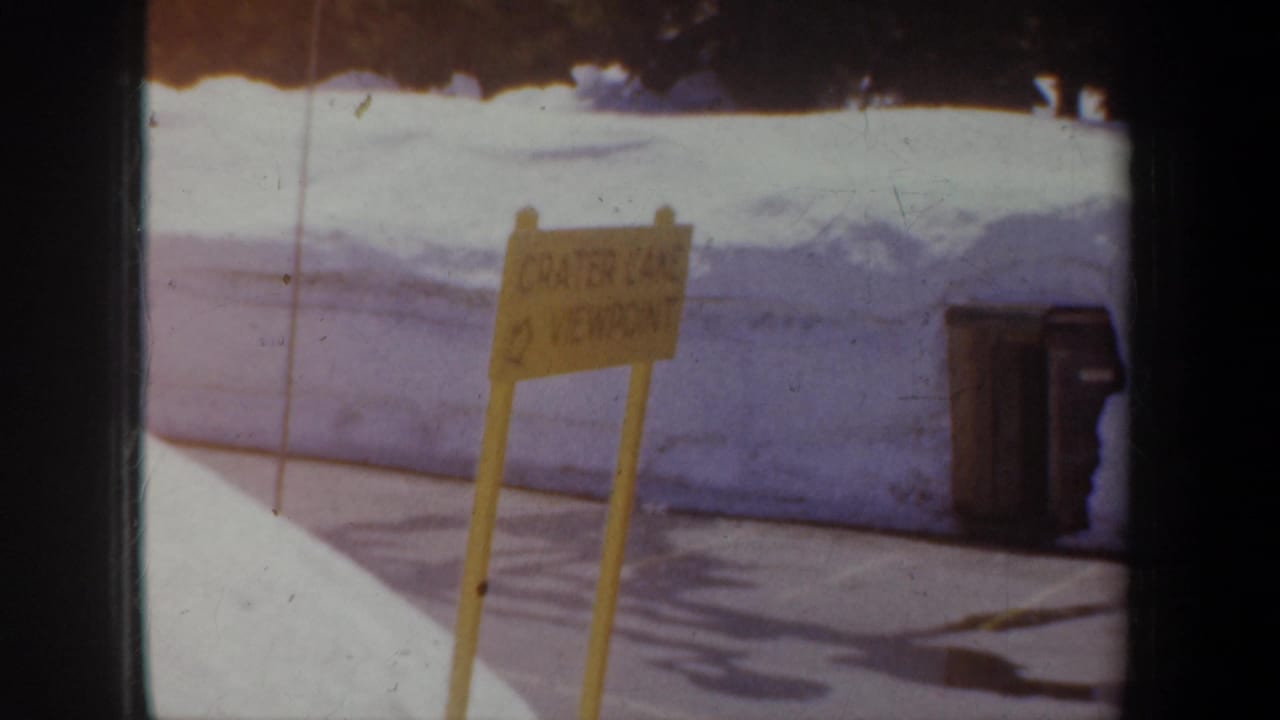 Yellow Crater Lake viewpoint sign with snowbank and trash can behind it.