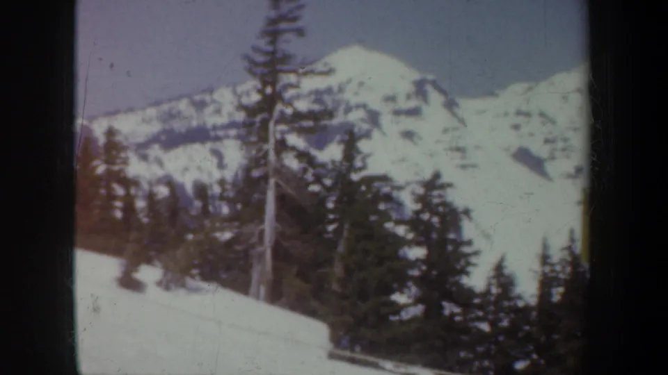 Vintage 8mm frame of a snow-covered mountain ridge and dark evergreens, consistent with the Crater Lake travel footage.