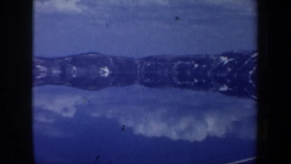 Blue-shifted 8mm frame from the Oregon winter clip showing a lake or river surface below a dark, snow-dusted ridgeline.