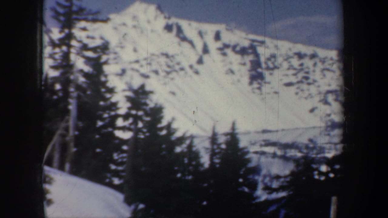 1957 Oregon home-movie frame showing a snowy mountain landscape with evergreens in the foreground and soft 8mm color fading.