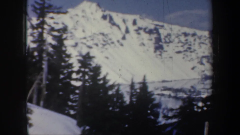 1957 Oregon home-movie frame showing a snowy mountain landscape with evergreens in the foreground and soft 8mm color fading.