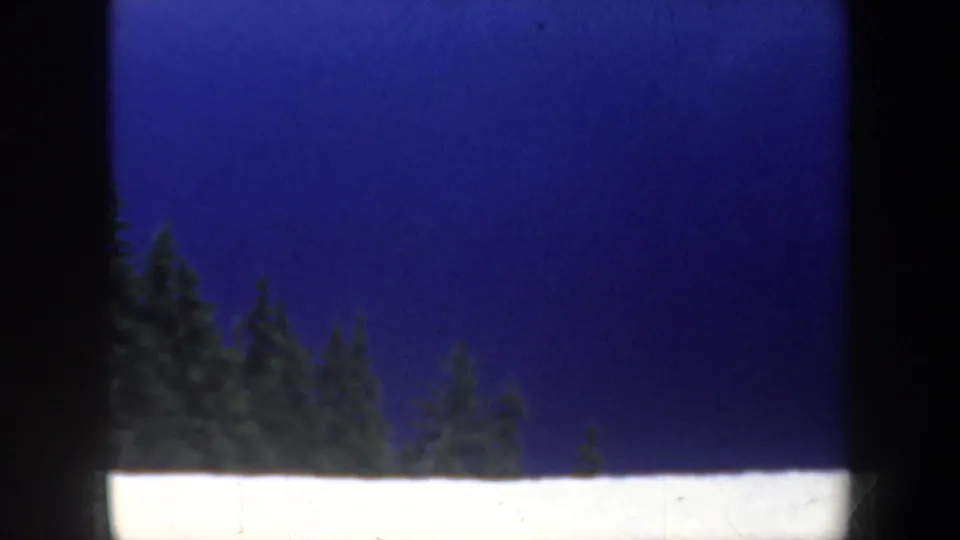1957 Oregon home-movie frame showing a dark blue sky or lake-like field above evergreen treetops and a strip of snow at the bottom edge.