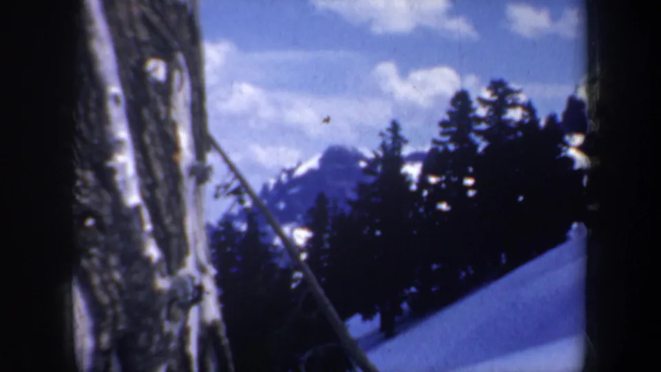 1957 Oregon 8mm frame with a close tree trunk, snowy hillside, dark evergreens, and mountain peaks beyond.