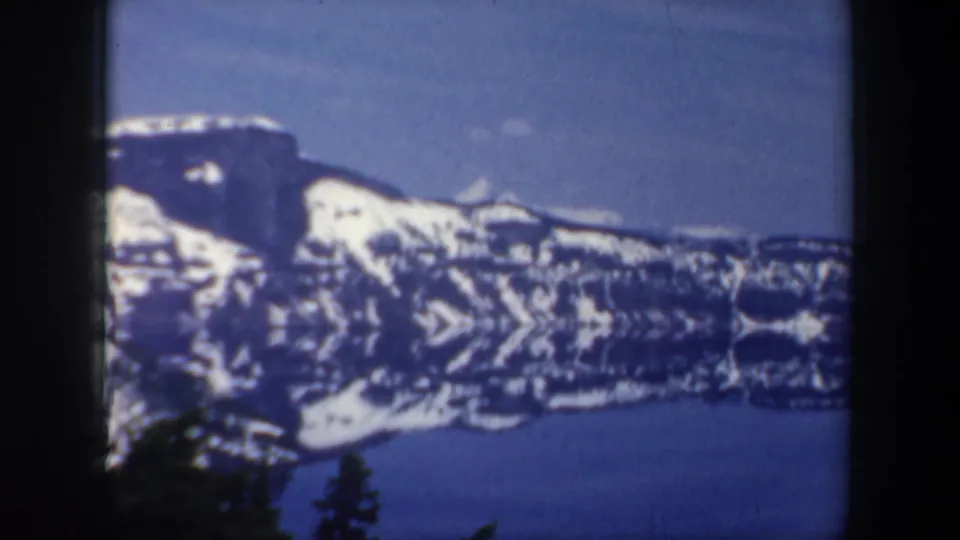 Mountain and lake vista from the 1957 home movie, with snowfields, reflected water, and silhouetted trees.
