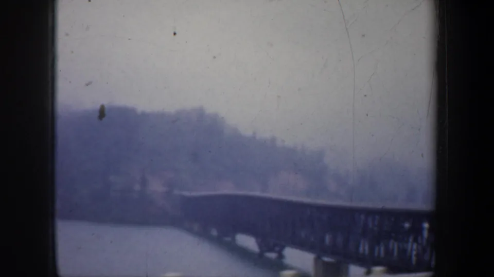 1957 Portland home-movie view of the railroad bridge stretching across the river beneath a wooded hillside.