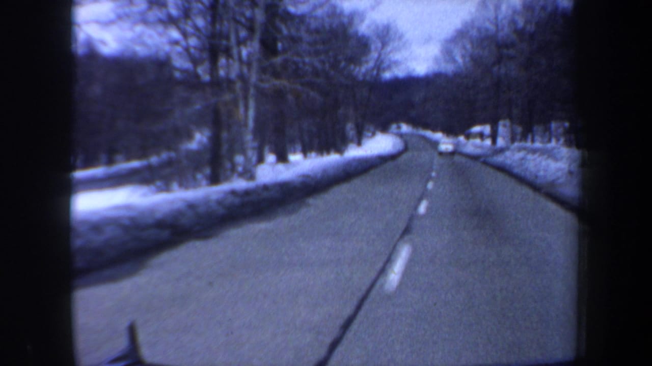 1962 New Hampshire 8mm view from a moving car on a snow-lined rural road with leafless trees and a distant vehicle.
