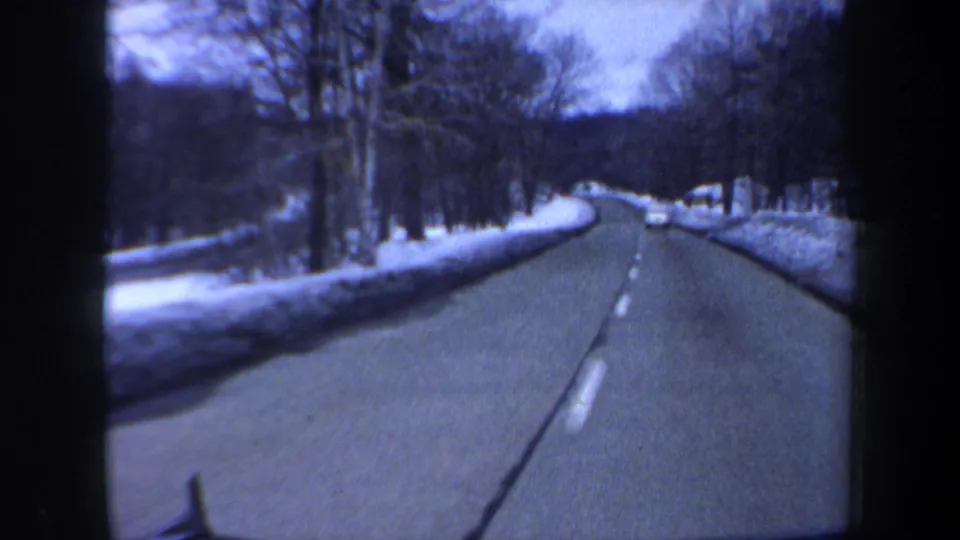 1962 New Hampshire 8mm view from a moving car on a snow-lined rural road with leafless trees and a distant vehicle.