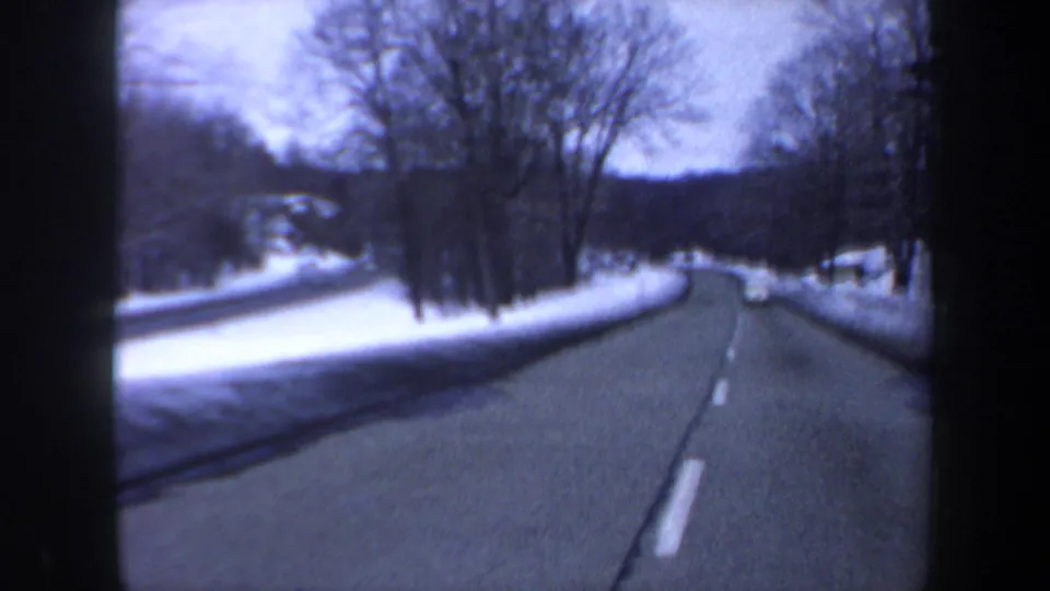 1962 8mm car-perspective footage shows a snow-edged New Hampshire road passing bare trees and low winter hills.