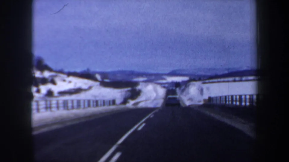 1962 New Hampshire 8mm view down a snow-lined two-lane highway with guardrails and a car in the distance.