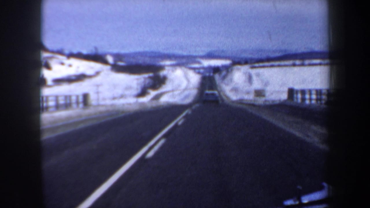 Snowy two-lane road with guardrails and a small car ahead.