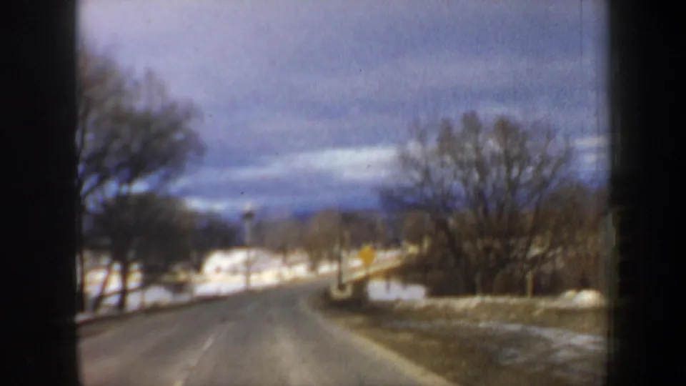 1962 New Hampshire road scene showing a gentle curve through snowy rural terrain under a cloudy sky.