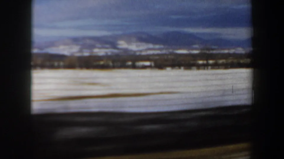 1962 New Hampshire rural landscape frame showing a broad snow-covered field, distant treeline, and low mountains on the horizon.