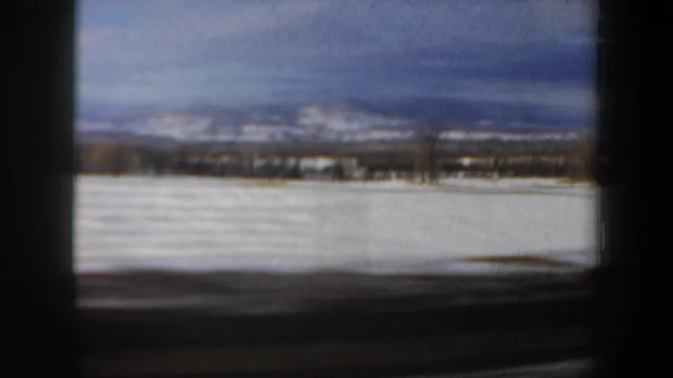 1962 New Hampshire home-movie frame of an open snowy field with a low mountain horizon and soft, overcast winter light.
