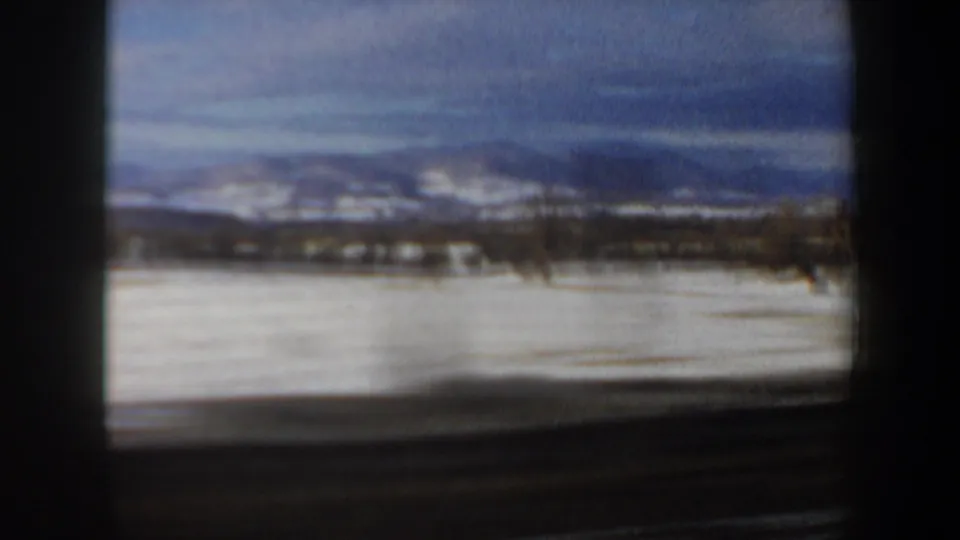 1962 New Hampshire 8mm frame showing snowy fields and distant hills or mountains from inside a moving car.