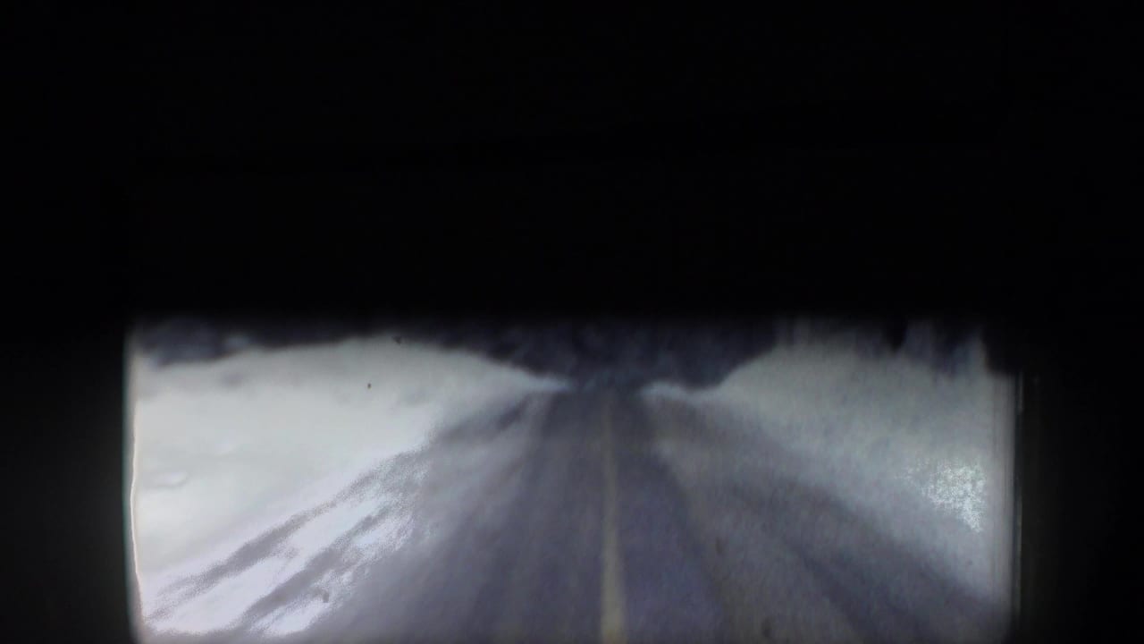 Blurred view of a snow-lined road ahead through a dark vehicle-framed opening.