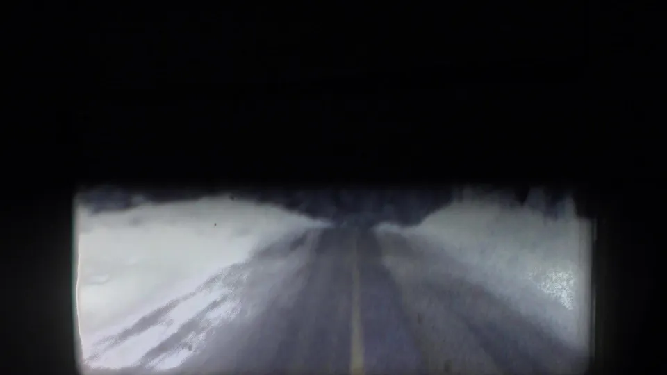 1962 New Hampshire winter road view, blurred by motion and framed by the dark interior edge of the car or film gate.