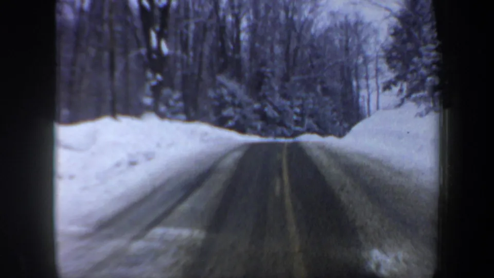 1962 New Hampshire 8mm frame of a plowed country road running through snow-covered forest and bare winter trees.