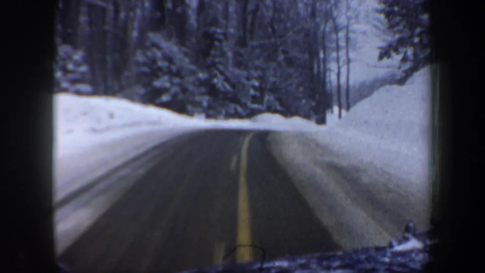 1962 New Hampshire winter driving frame showing a plowed road curving through snowy woods with high roadside banks.