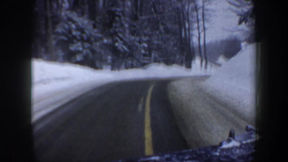 1962 New Hampshire home-movie view from a moving vehicle on a snow-lined forest highway with yellow center markings.
