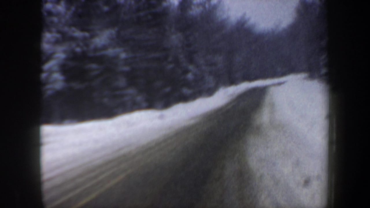 1962 New Hampshire 8mm view of a snow-covered winding road with dense roadside trees and high winter snowbanks.