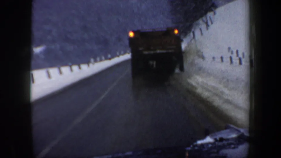Rear-facing 1962 New Hampshire 8mm view of a large truck traveling along a snowbank-lined mountain road.