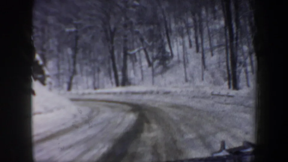 1962 New Hampshire winter road scene from a moving car, showing a curved snowy roadway through a wooded area.