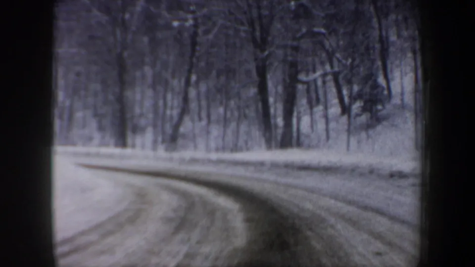 1962 New Hampshire 8mm driving view of a snow-lined curve through a wooded roadside, with soft motion blur from the moving car.