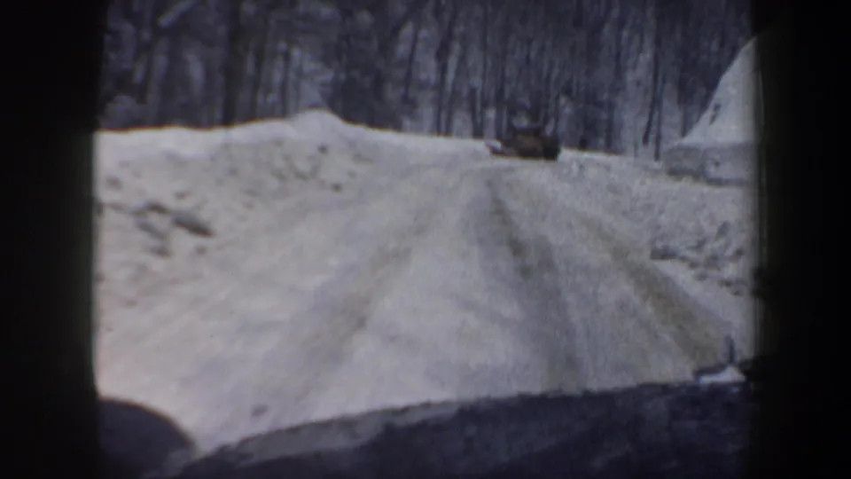 1962 New Hampshire 8mm view from inside a vehicle following a plow or truck along a snowy wooded road.