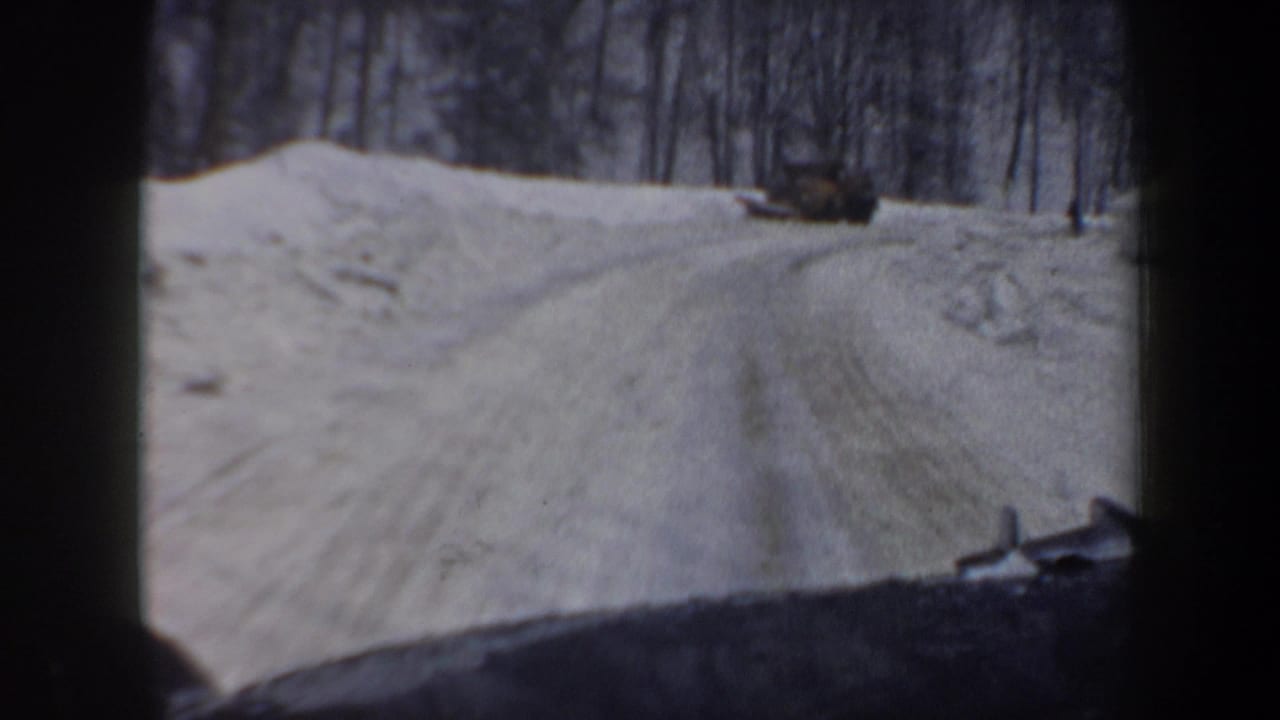 1962 New Hampshire winter road footage shows a snow-packed lane through trees with a plow or vehicle ahead.
