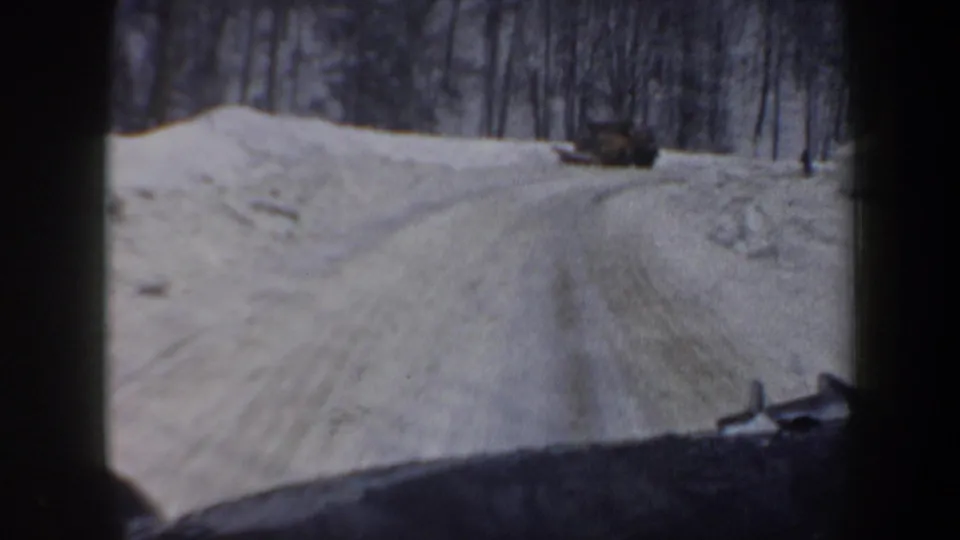 1962 New Hampshire winter road footage shows a snow-packed lane through trees with a plow or vehicle ahead.