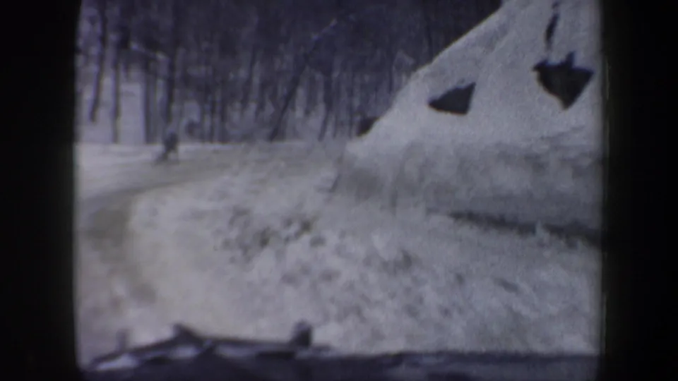 1962 New Hampshire winter road view from inside a vehicle, with a small figure walking near the snowy roadside.
