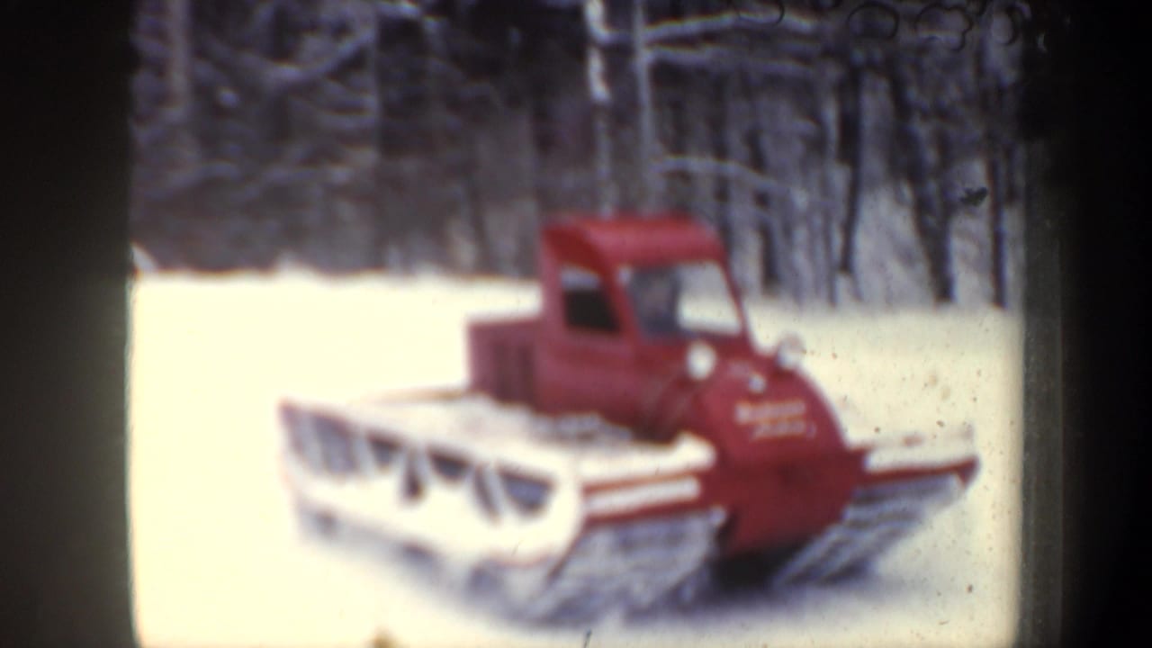 Red tracked snow vehicle on a snowy forest road, seen in soft focus from the front side.