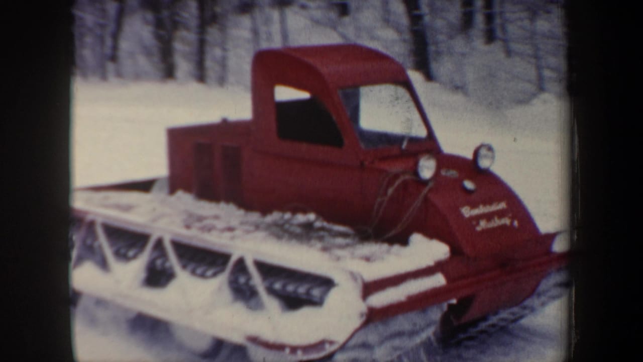 1962 New Hampshire home-movie frame with a red tracked snow vehicle and partial lettering on its nose in deep snow.